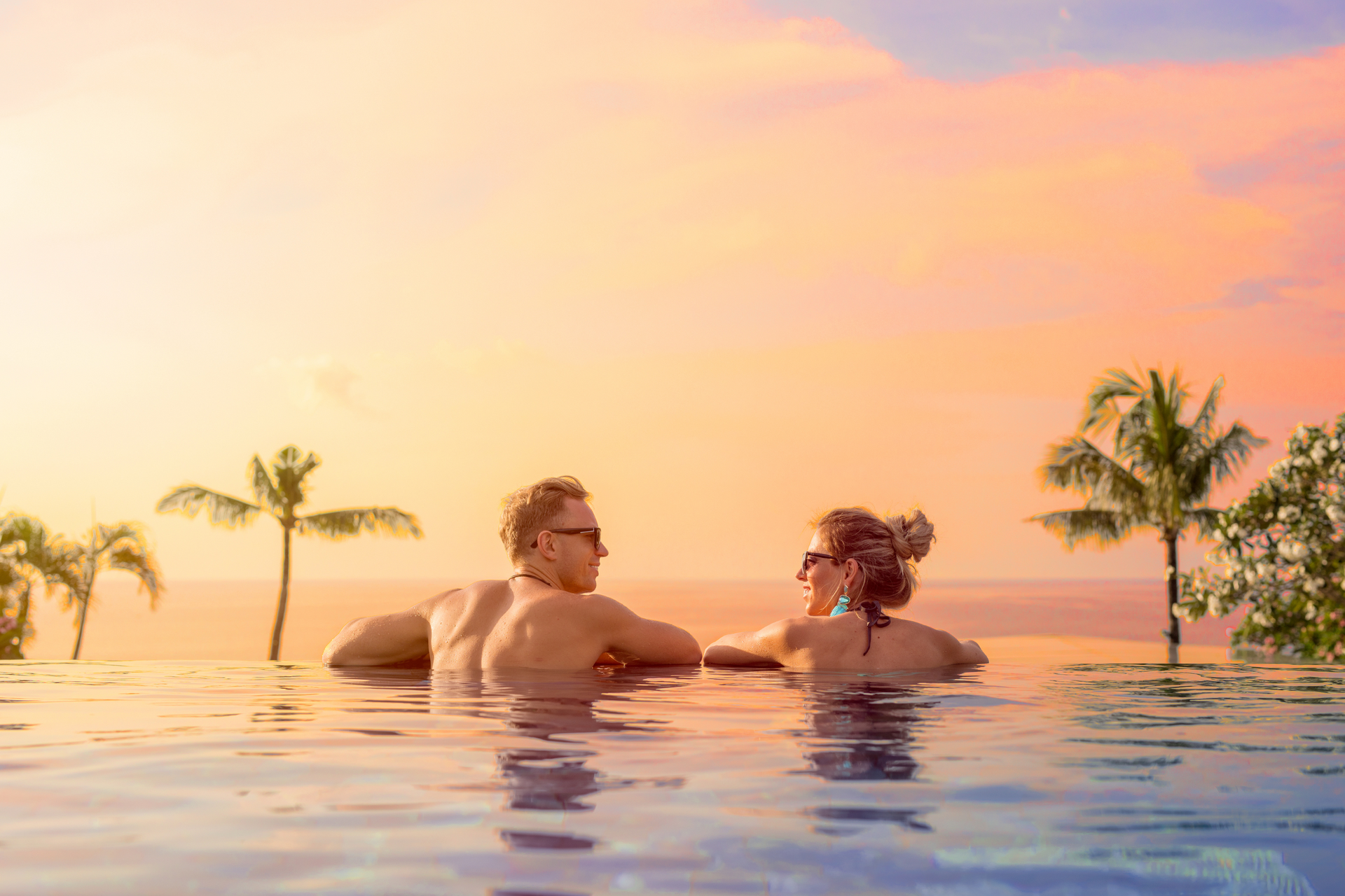 A man and a woman are sitting in an infinity pool at sunset.