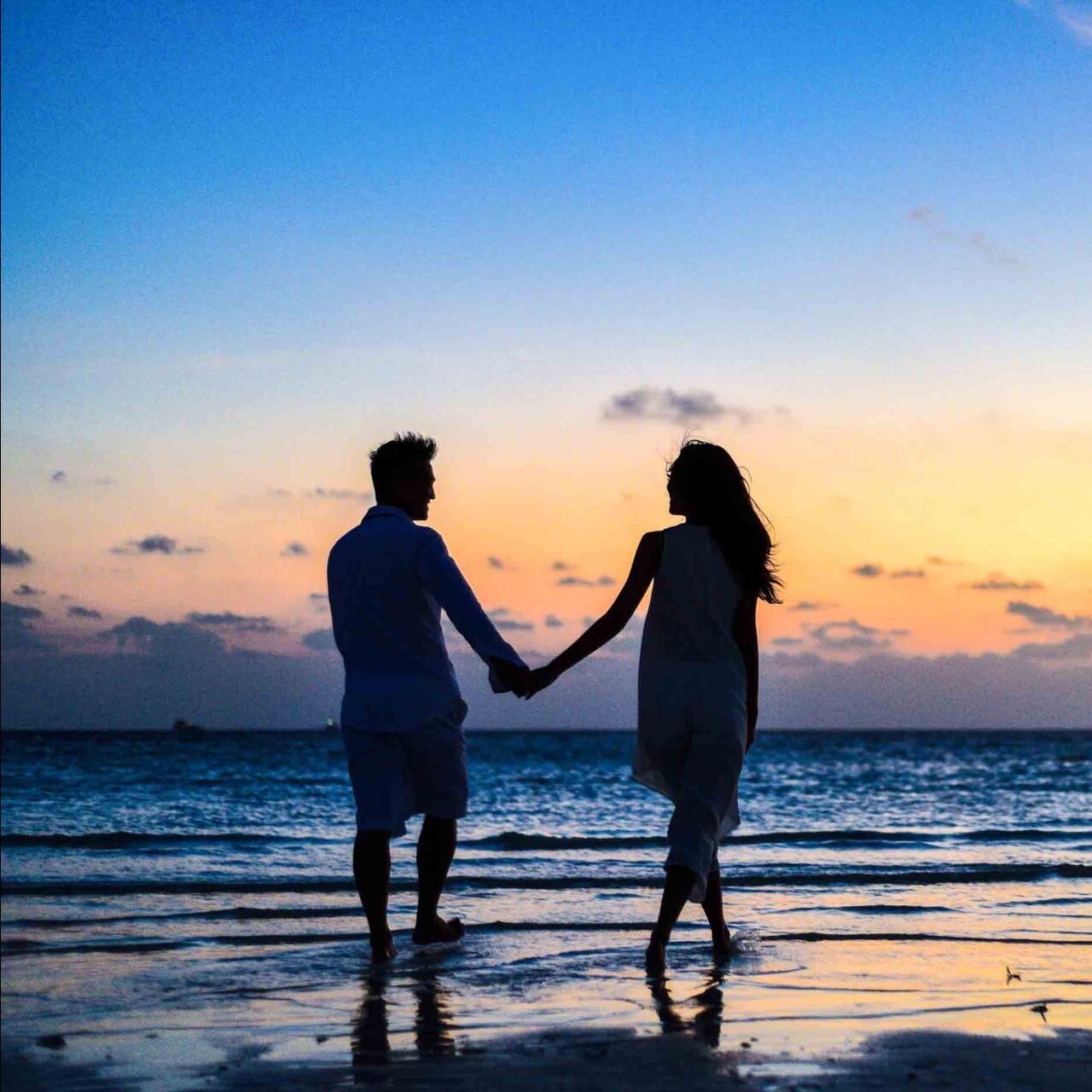 A man and a woman are holding hands on the beach at sunset.
