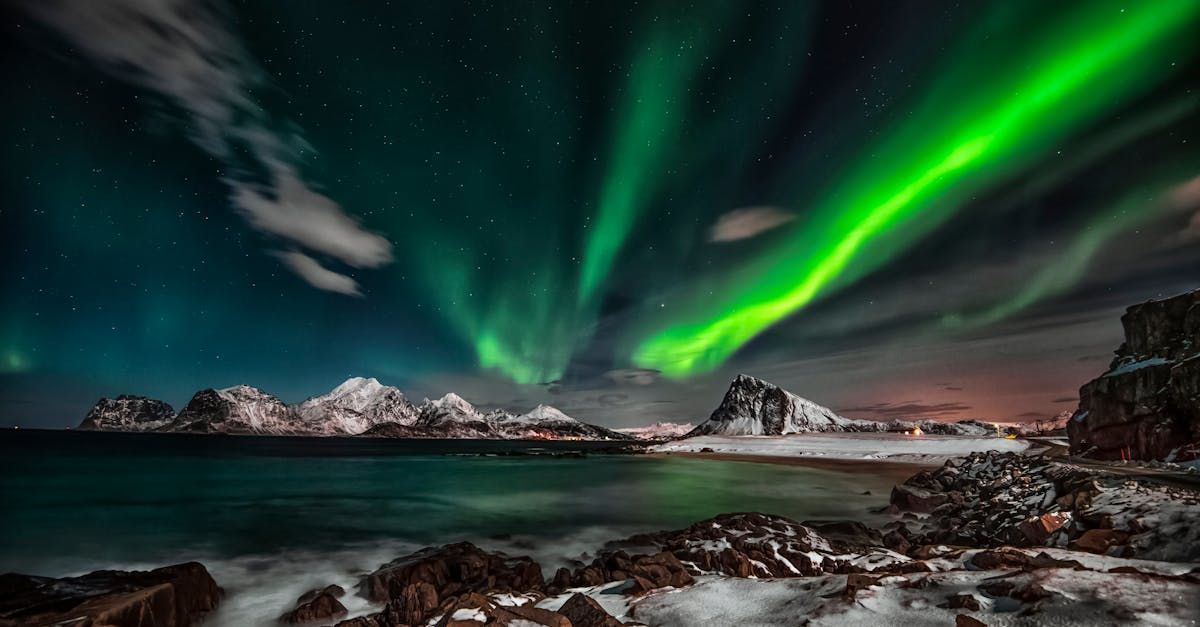 The aurora borealis is shining over the ocean and mountains.