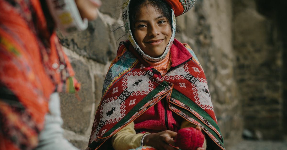 A young girl wearing a blanket and a hat is sitting next to a woman.