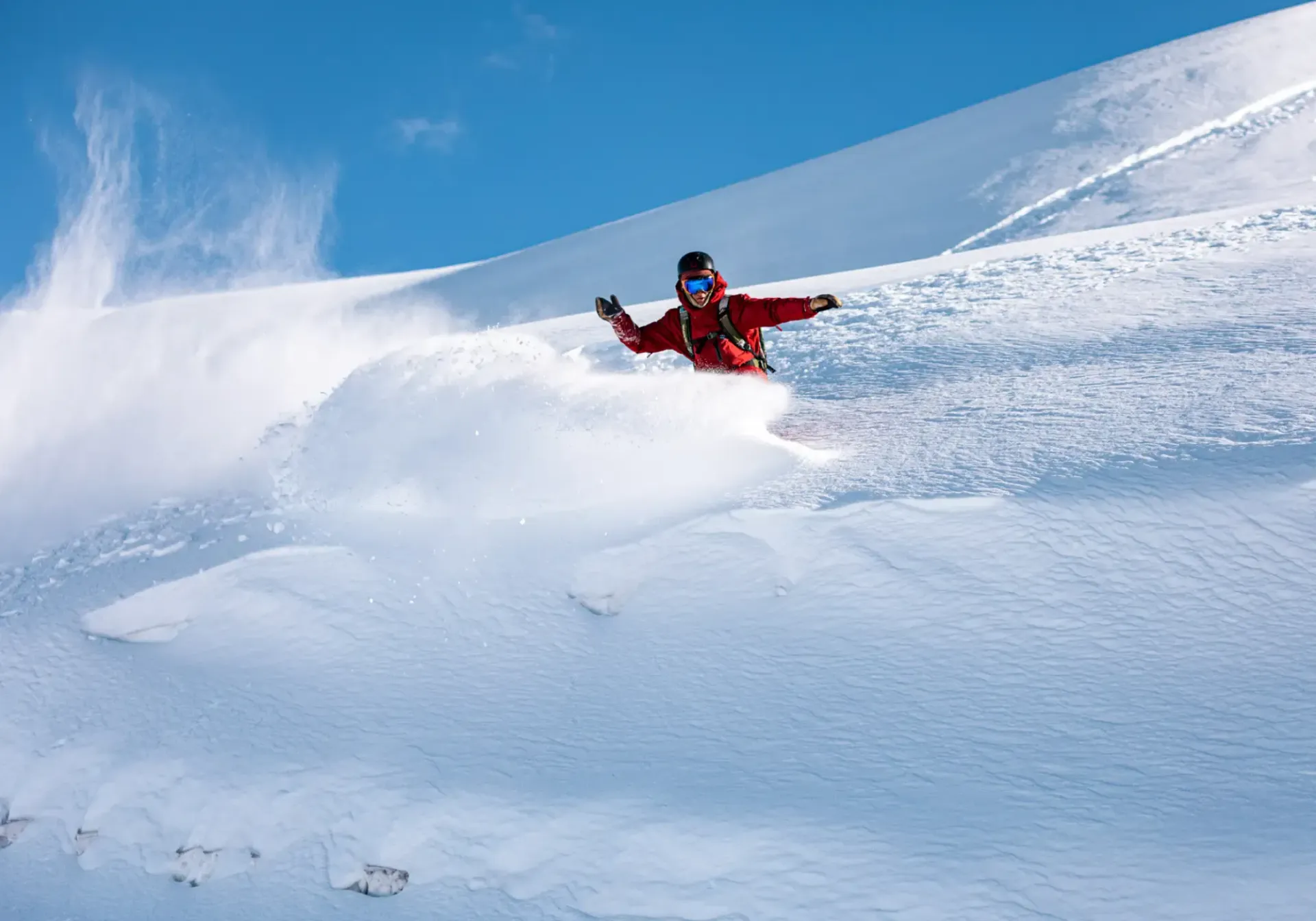 Skier in a red jacket carving through deep powder on a snowy mountain slope