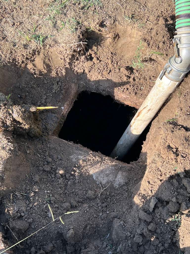 Open dirt hole in the ground with a pipe entering from the right side.