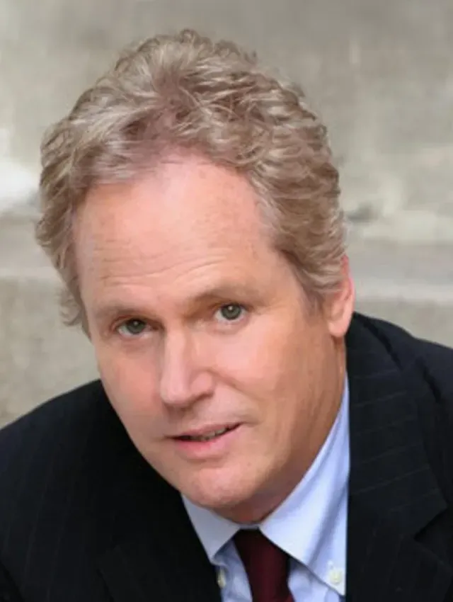 Head-and-shoulders portrait of a man in a dark suit and red tie, with gray hair and a slight smile.