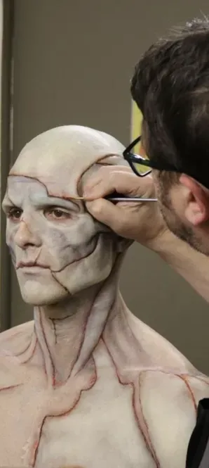 Artist painting facial details on a realistic bald bust with red guide lines