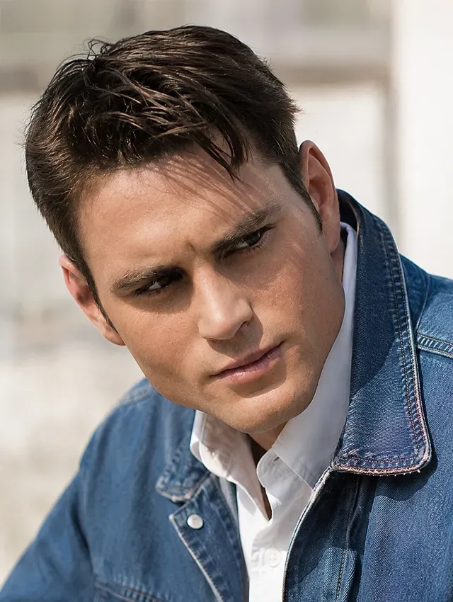 Man in a denim jacket looking downward against a blurred outdoor background