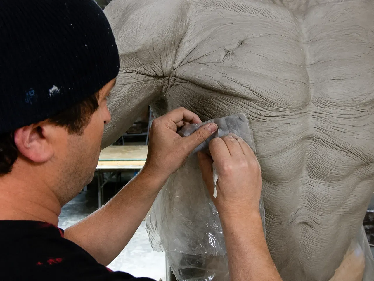 Person hand-paints a large white mural outdoors, working on a detailed section with a brush.