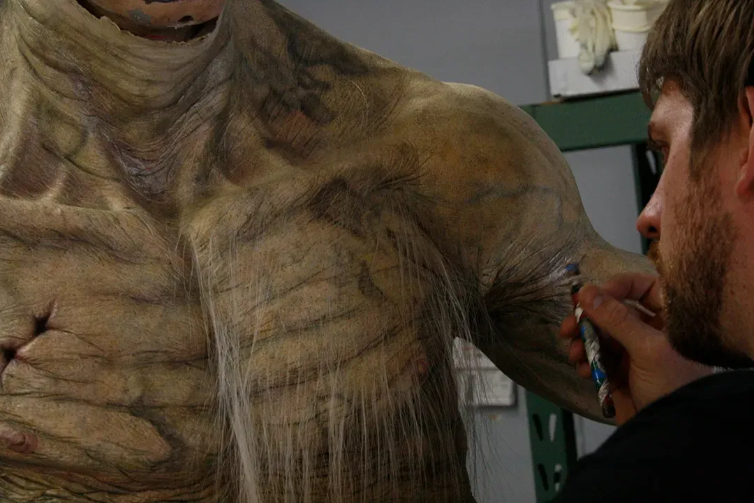 Person applying makeup to a large creature costume on a film set