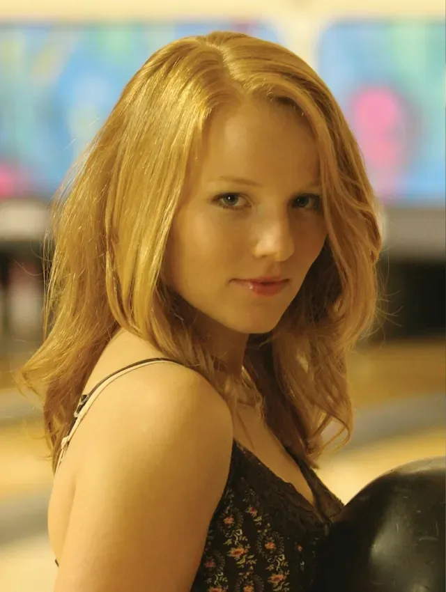 Woman with red hair holding a black bowling ball in a bowling alley