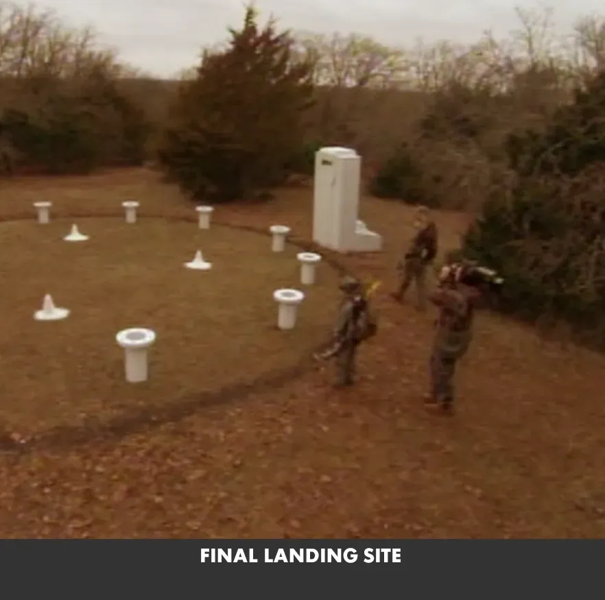 People near a labeled final landing site with white markers on a brown field and trees nearby