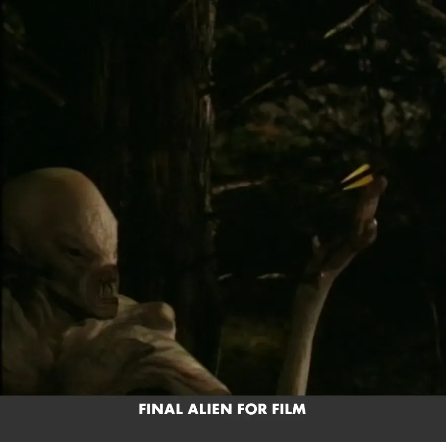 White alien in dark forest holding up a glowing yellow object, with “FINAL ALIEN FOR FILM” caption below