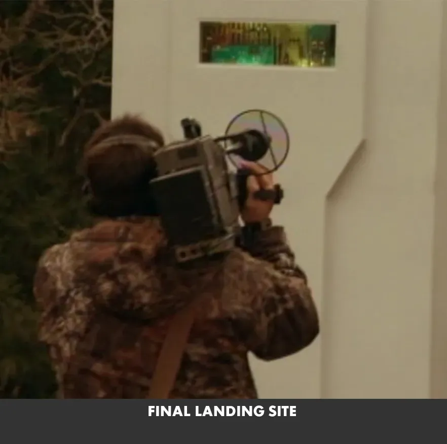 Person in camouflage holds a camera to a wall opening labeled “FINAL LANDING SITE.”