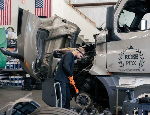Mechanic working on a large damaged truck in a garage, with the hood open and tools nearby