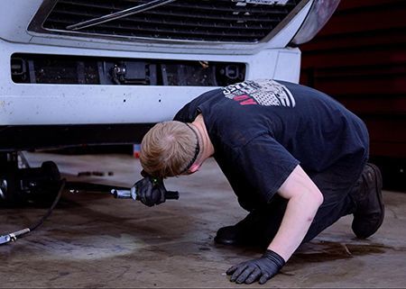 Mechanic in black gloves working under a white car in a garage