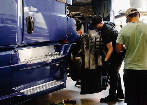 Two workers load luggage into a blue tour bus at a service bay.