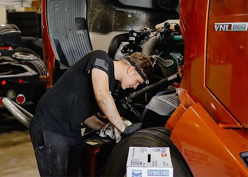 Mechanic working on a truck engine in a garage, leaning into the open hood