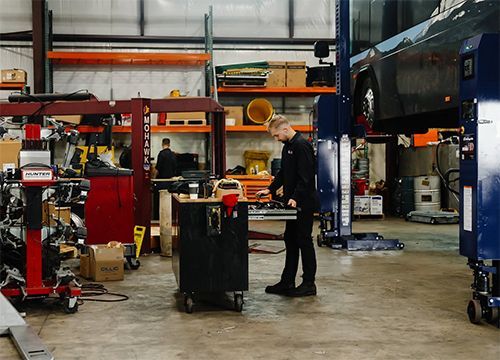 Person in a workshop surrounded by machinery and tools, standing beside a black workbench.