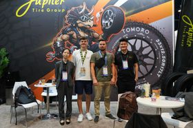 Four people posing at an event booth with a tire-themed backdrop and tables on either side