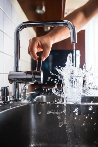 Hand turning on a kitchen faucet, water splashing into a black sink