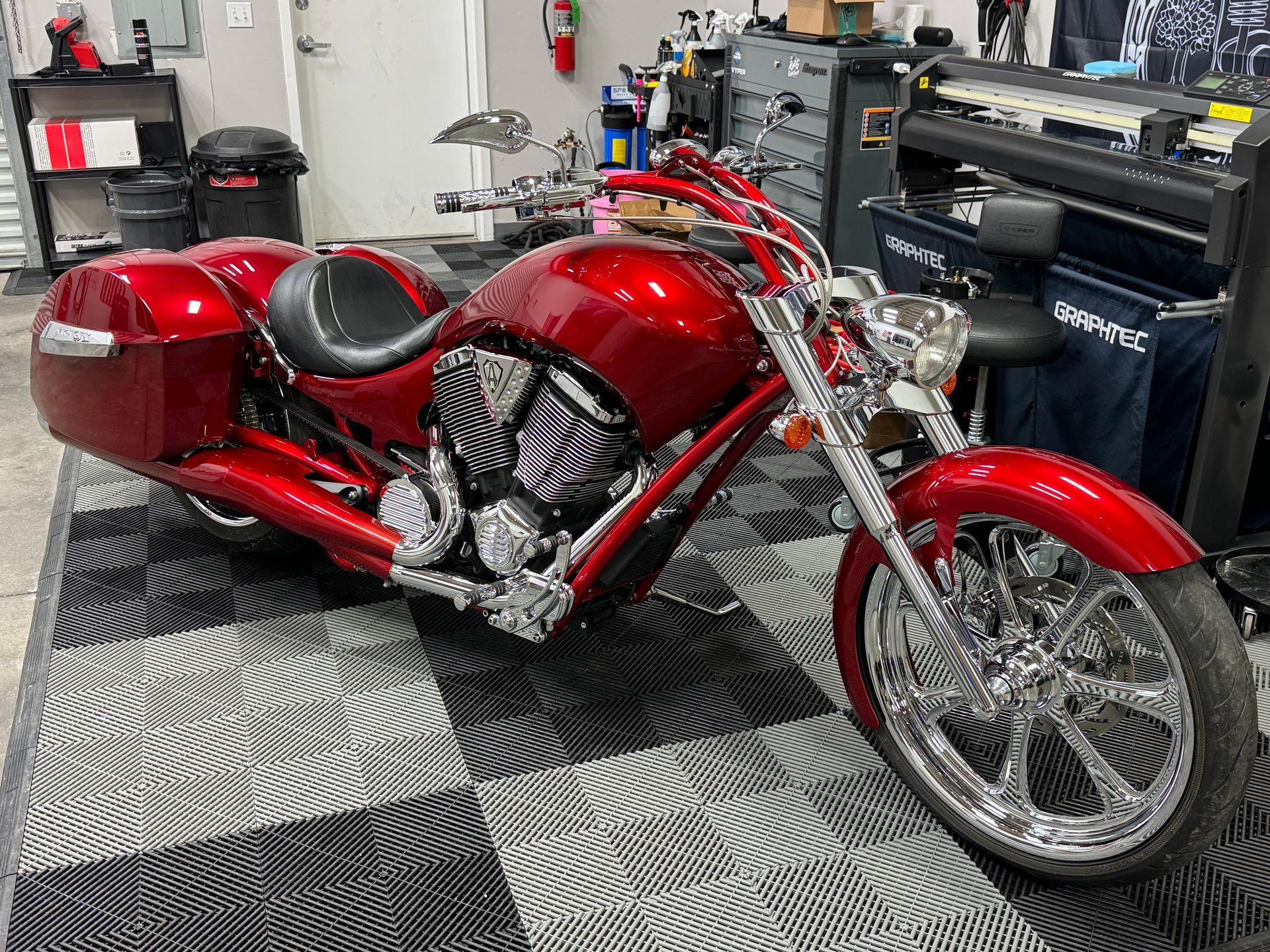 A red motorcycle is parked on a checkered floor in a garage.