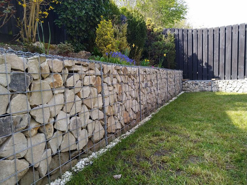 A Stone Wall In A Garden With A Black Fence In The Background — DCK Concreting In Lake Cathie, NSW