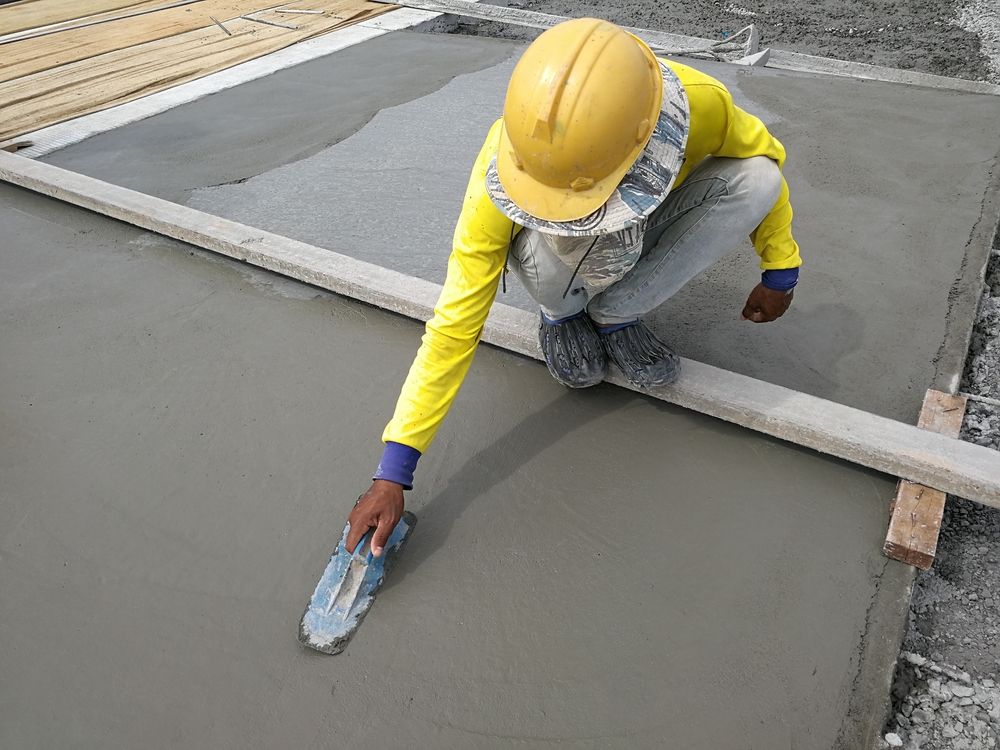 A Construction Worker Is Kneeling Down And Spreading Concrete With A Trowel — DCK Concreting In Laurieton, NSW