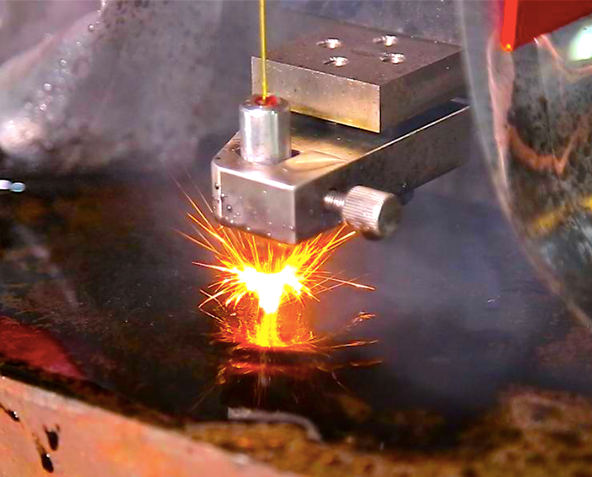 En un taller industrial, un cabezal de corte láser emite chispas de color naranja brillante 
