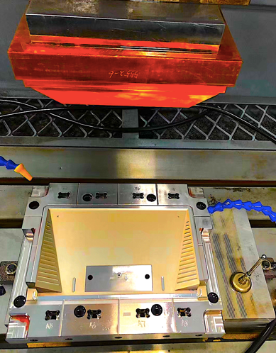 Un molde industrial de metal reposa sobre la bancada de una máquina; presenta una gran cavidad interior de color dorado