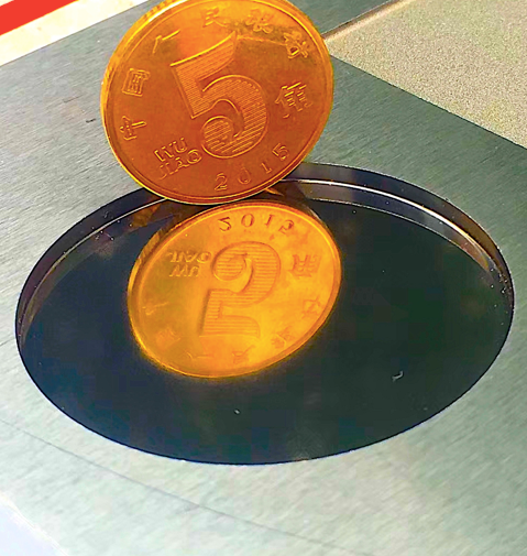 Una moneda de oro de 5 jiao reposa sobre una superficie metálica, proyectando un reflejo que parece una moneda de 2 jiao.