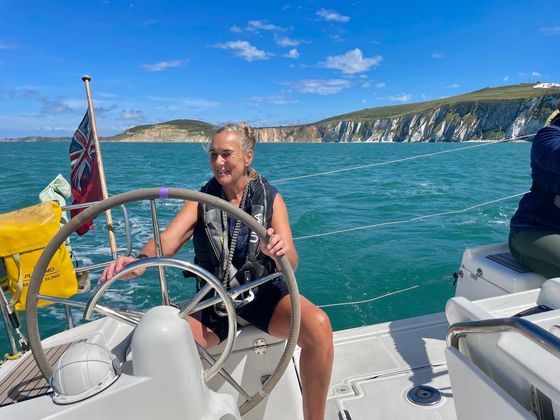 Picture of a female VI sailor smiling and steering a wheel with white cliffs in the background
