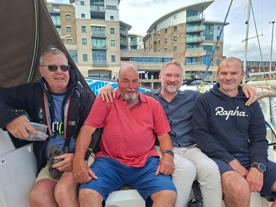 Four men both sighted and VI sat on the cockpit bench arms round each other smiling with Poole town in the background