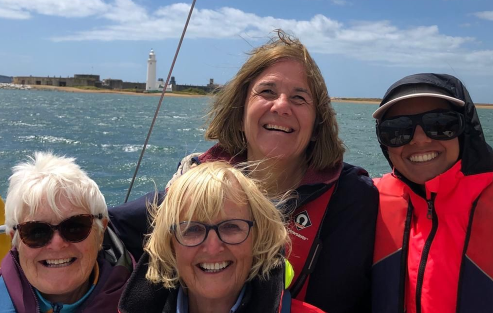 A close up of four female crew members both sighted and VI smiling with Hurst Castle in the background. A close up of four female crew members both sighted and VI smiling with Hurst Castle in the background.