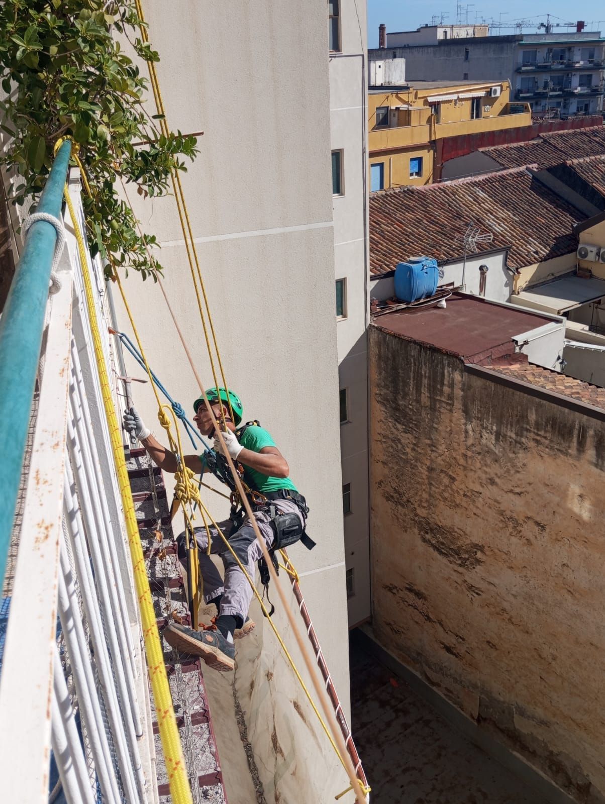 Uomo che si cala in corda doppia da un edificio, indossando l'attrezzatura di sicurezza, con un paesaggio urbano sullo sfondo.