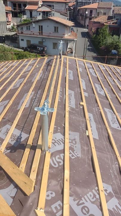 Costruzione del tetto: travi in ​​legno e strato di impermeabilizzazione. Un tubo di sfiato si estende verso l'alto. Case e strada visibili sullo sfondo.