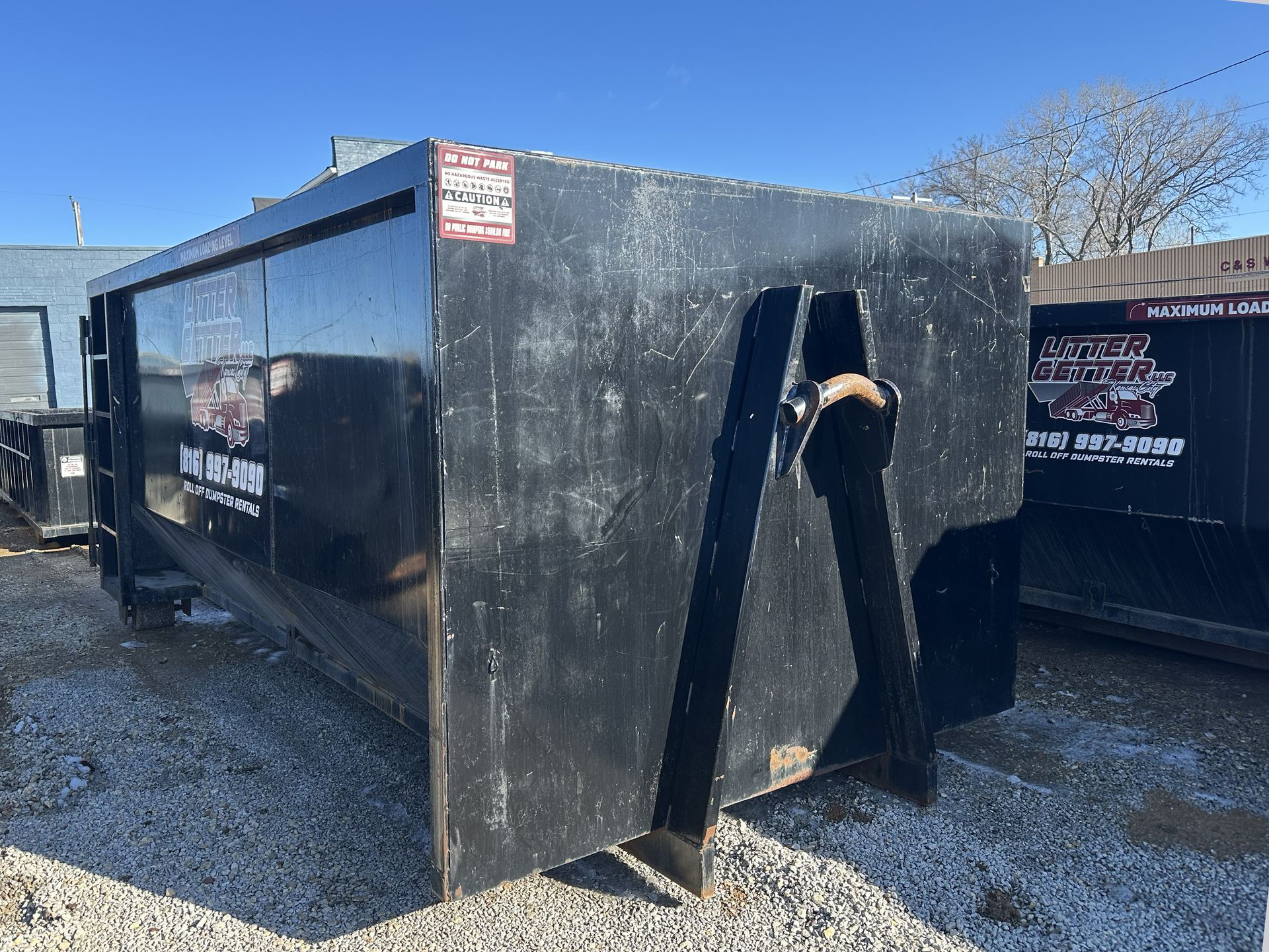 Black Litter Getter dumpster with lifting arms, parked on gravel in Kansas City