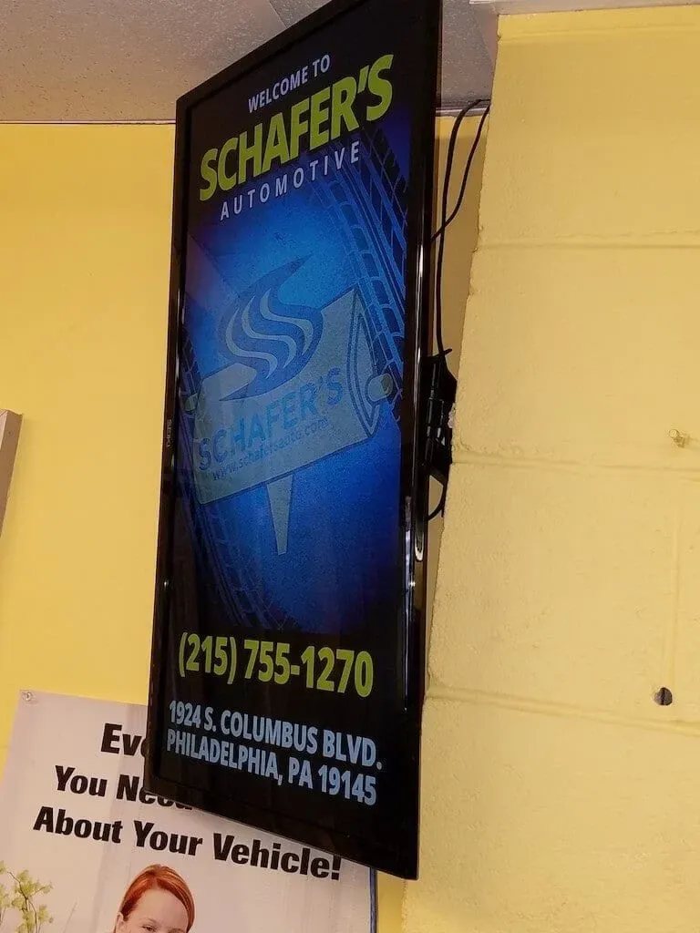 Vertical blue Schaefer's Towing sign on a yellow wall with phone number and Los Angeles address.