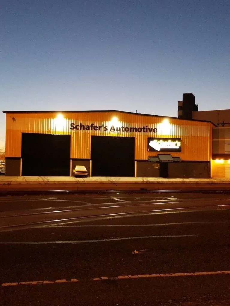 Schaffer’s Automotive storefront at dusk with lit orange siding and dark empty parking lot