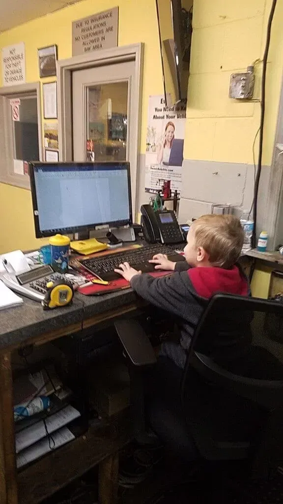 Person seated at a desk using a computer in a cluttered office workspace.