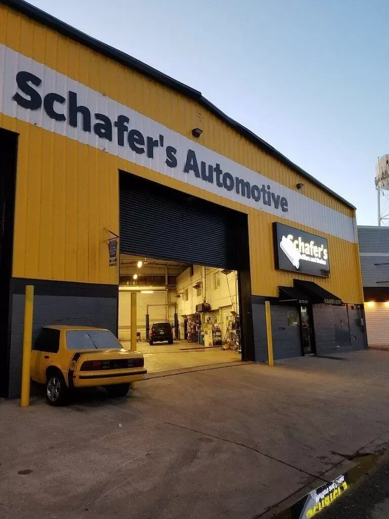 Scharer's Automotive garage with yellow exterior, open service bay, and a yellow SUV parked outside
