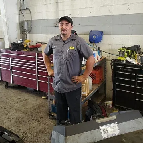 Mechanic standing in an auto repair shop beside red tool cabinets and a workbench