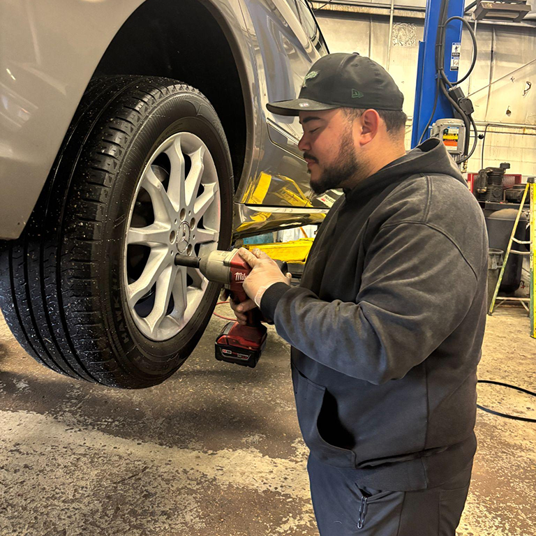 Mechanic using a power tool to work on a car wheel in an auto repair shop