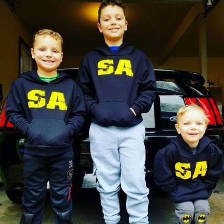 Three boys in navy SA hoodies posing in a garage in front of a black vehicle