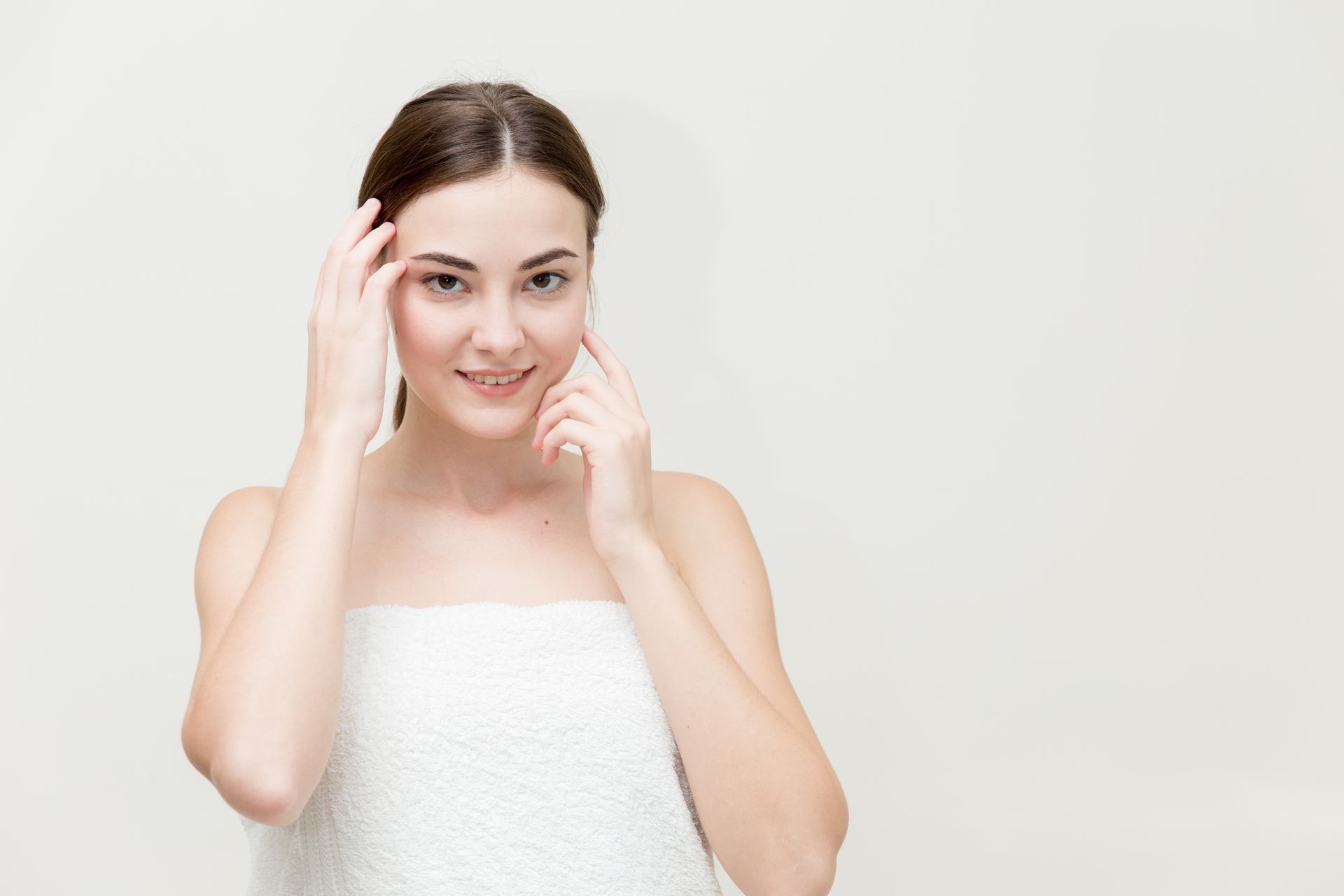 Woman with a towel on her shoulders touching her face against a white background