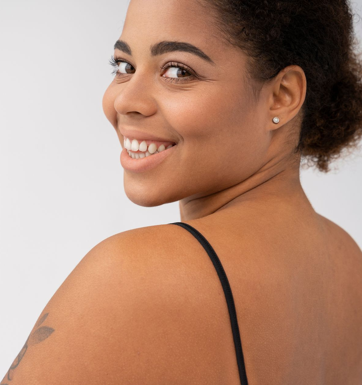 Smiling person in a black strap top looking over their shoulder against a light background