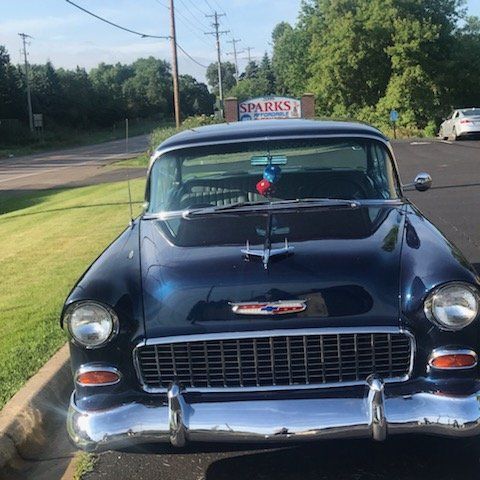 Dark blue vintage Chevrolet parked in front of Sparks business sign on a sunny day.