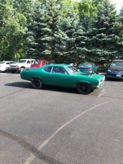 Green classic car parked on asphalt, trees in background.