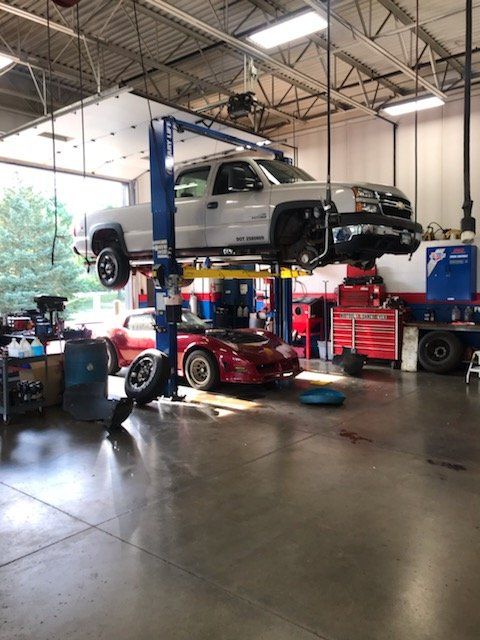 A truck on a lift inside a garage, a red car is beneath it.