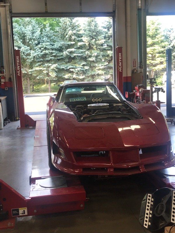 Red Corvette on a lift in a garage with the hood open.