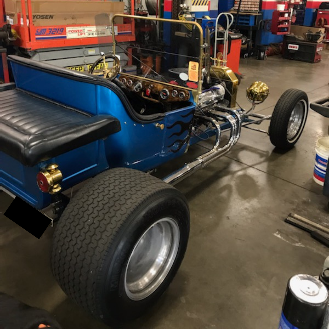 Blue hot rod car with flames on the side, large rear tires, and chrome details inside a garage.