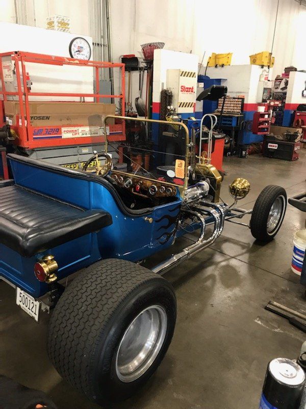 Blue and chrome hot rod in a garage, with large rear tires and exposed engine.