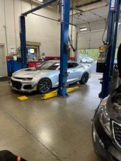 Silver sports car raised on a lift in a repair shop.